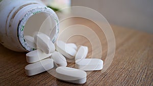 White pills spilling out of a bottle on textured wooden background. Heap of calcium pile and tablets. Medicines, antibiotic, ,