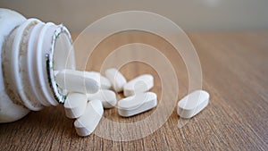 White pills spilling out of a bottle on textured wooden background. Heap of calcium pile and tablets. Medicines, antibiotic, ,