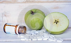 White Pills Spilling Out of a Glass Pill Bottle and Green Apples .Diabete Concept photo