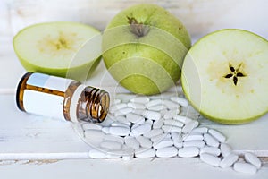 White Pills Spilling Out of a Glass Pill Bottle and Green Apples .Diabete Concept photo