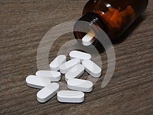 White pills spilling out of a pill bottle on wooden table