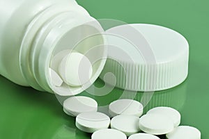 White pills spilling out of a toppled white pill bottle on green background