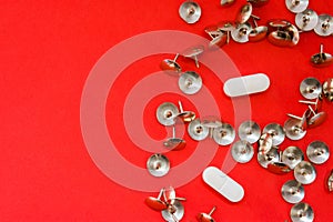 White pills surrounded by sharp thumbtacks at distance from them is on red background with empty area for headers top view. Concep
