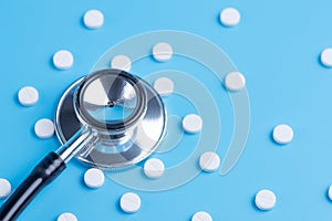 White pills or tablets and stethoscope on blue background