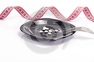 White pills for weight loss and supplements like food on a black plate with a fork and a pink tape. Diet pills and supplements,