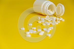 White pills and white bottle on a bright yellow background, healthy and medicine concept.