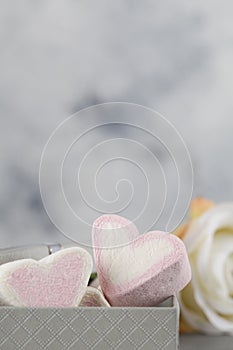 White and pink candy in form of hearts in box on gray background with flower. Valentines day minimalism background
