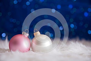 White and pink Christmas balls on fur with garland lights on blu