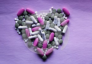 White, pink and green pills laid out in the shape of a heart on a pink background. multi-colored drugs. concept - heart disease, h