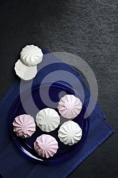 White and pink marshmallow on blue plate on black background