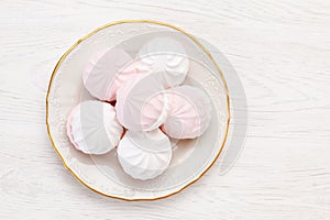 White and pink marshmallow zephyr lies on a white plate on a wooden table