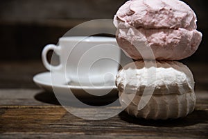 White and pink marshmallows and a cup of coffee on a wooden table