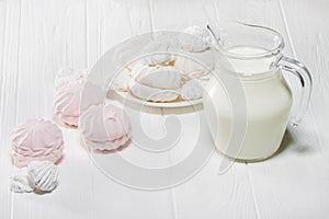 White and pink marshmallows and a jug of milk on a white wooden table. Food