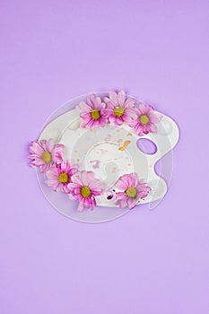 White plastic artist palette with violet daisies in it. Creativity concept