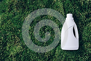 White plastic bottle of cleaning product, household chemicals or liquid laundry detergent on green grass, moss