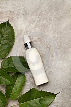 A white plastic bottle and green leaves on a gray marble countertop