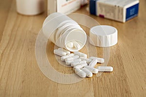 White plastic bottle for medicines. Scattered pills and drug boxes in the background.