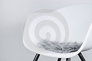 Side view of a modern white plastic chair with a seat cushion made of grey artificial long fur, use as design background for