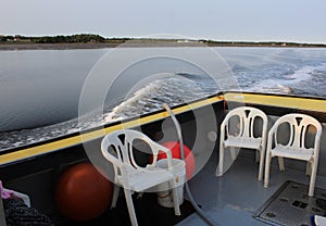 White plastic chairs sitting in the back of a yellow and black fishing boat on the calm waters of a bay in Nova Scotia