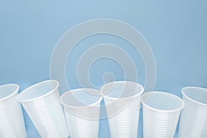 White plastic empty cups laid out in a row on blue background.