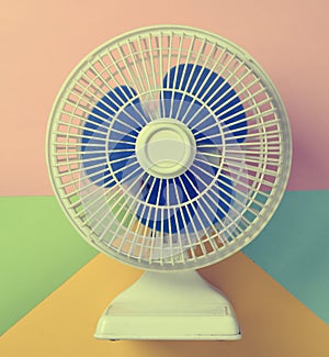 White plastic fan with blue louvres on a multicolored pastel photo