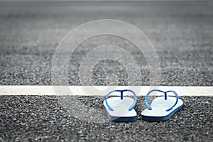 White plastic flip flop shoe on black asphalt road