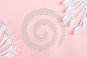 White plastic forks and spoons lie on the sides on a light pink background