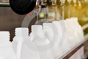 White plastic gallons or bottles on the production line of the conveyor at filling machine in the factory with sunbeam in the