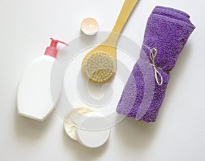 White plastic jars with creams, purple towel, candle, brush for dry massage. The concept of Spa, body care. Top view