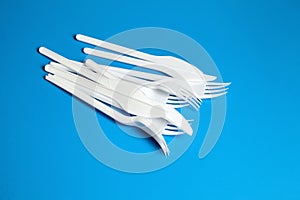 White plastic knives and forks. Disposable plastic tableware on blue background