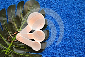 White plastic measuring spoons lie on a palm leaf on a blue cloth background