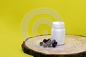 White plastic medical container with dry rosehip fruits on wooden board on yellow background, mockup. Blank Medicine bottle.