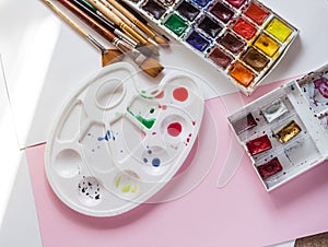 palette with a set of watercolor paints and brushes on a pink background, the artist`s tools