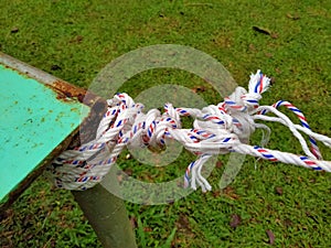 White plastic rope tied and knotted at the end of the green iron table pole.