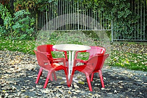 White plastic table with red chairs in a cafe in the autumn park. Closing season