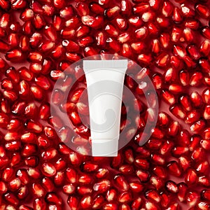 White plastic tube with pomegranate cream on red ripe garnet seeds. Natural organic cosmetic product packaging design, branding