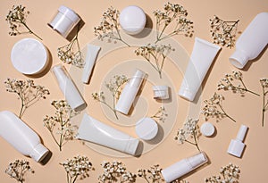 White plastic tubes, jars, and gypsophila branches on a beige background, containers for cosmetic creams and gels, advertising and