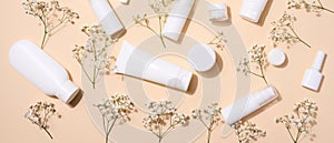 White plastic tubes, jars, and gypsophila branches on a beige background, containers for cosmetic creams and gels, advertising and