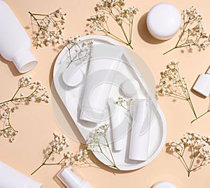White plastic tubes, jars, and gypsophila branches on a beige background, containers for cosmetic creams and gels, advertising and