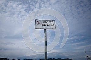 White plate against cloudy sky that says Divieto di Pesca means Fishing prohibited in Italia photo