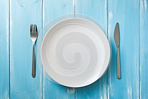 White Plate on blue wooden background with utensils