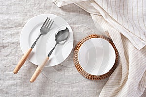 White plate and bowl with spoon, fork and linen napkin on tablecloth