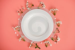 White plate and branches of cherry blossoms on pink background, top view, copy space