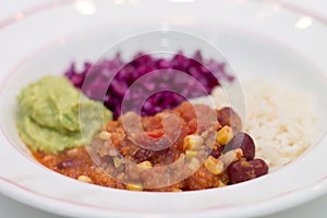 White plate of chili sin carne with red cabbage, guacamole and r