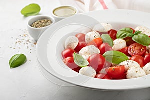 White plate of classic delicious caprese salad with ripe tomatoes, mozzarella and fresh basil leaves on gray background. Italian f