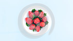 White plate is filled with beautiful juicy red strawberries with beautiful green leaves. Summer concept