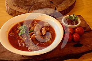 A white plate, filled with chicken gizzards in tomato sauce, on a wooden board, garnished with a parsley leaf and red sauce in a