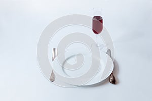 White plate with fork, knife and glass of champagne on a white background