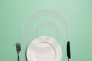 A white plate with fork and knife on green background with copy space.