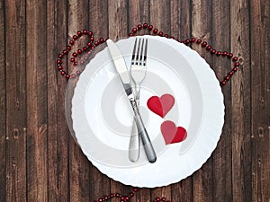 White plate, fork, knife, heart wooden background
